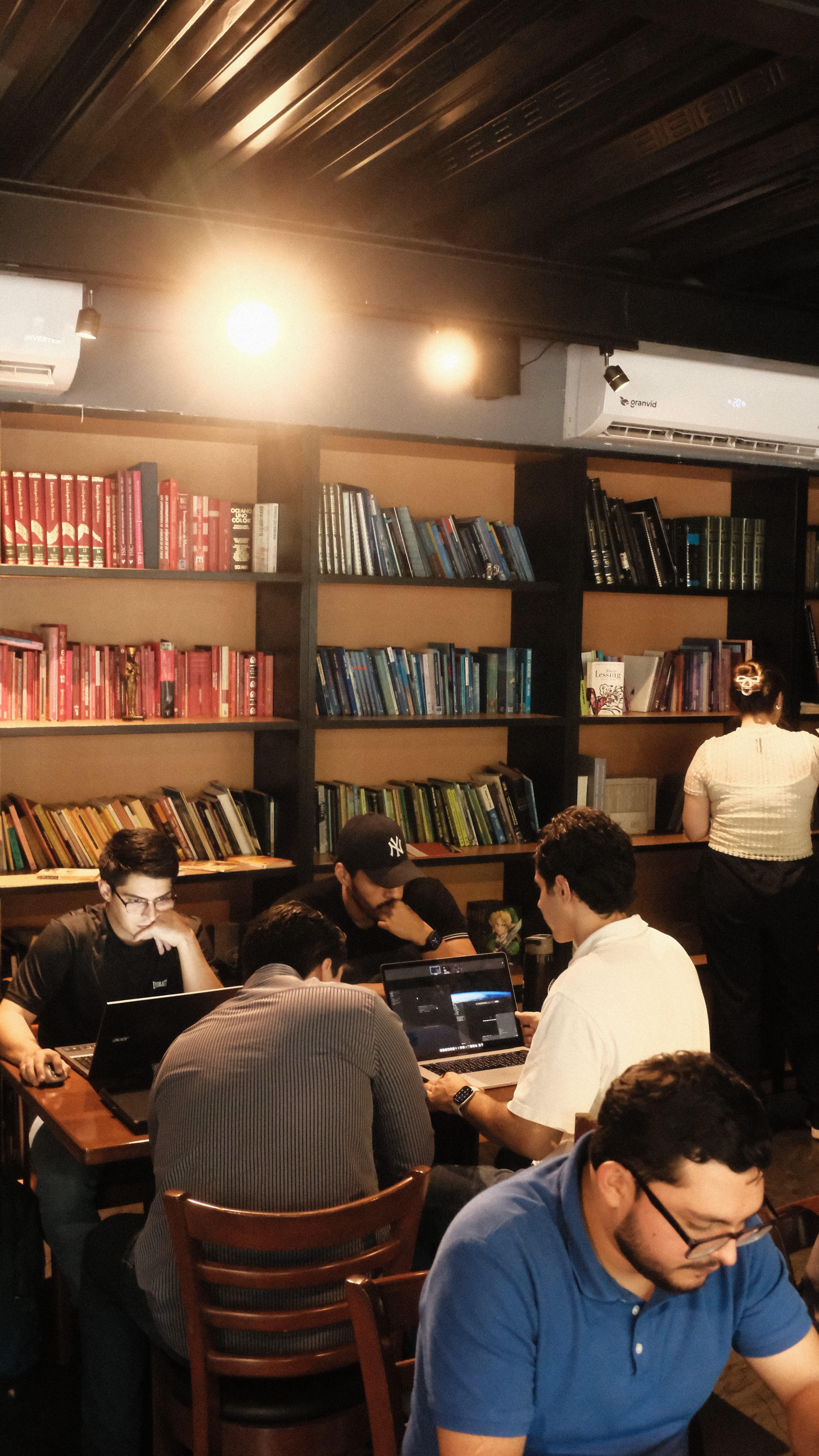 Builders working on laptops in front of bookshelves at Cafe Cursor Culiacán